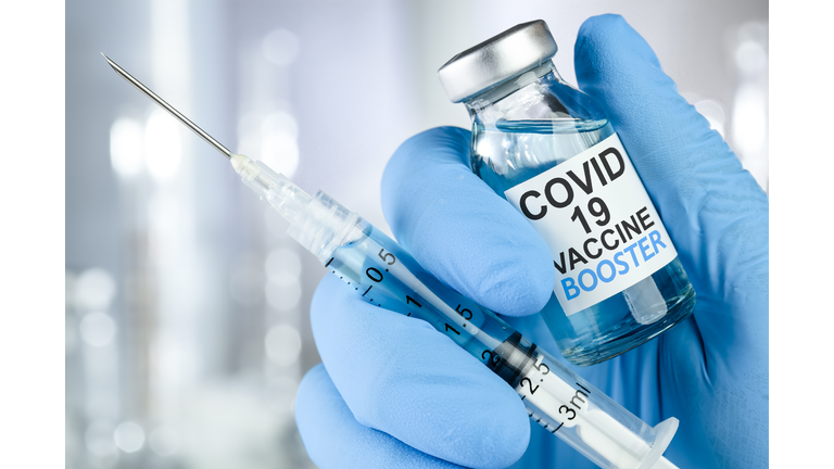 Hand in blue medical gloves holding a syringe and vaccine vial with Covid 19 Vaccine Booster text, for Coronavirus booster shot.