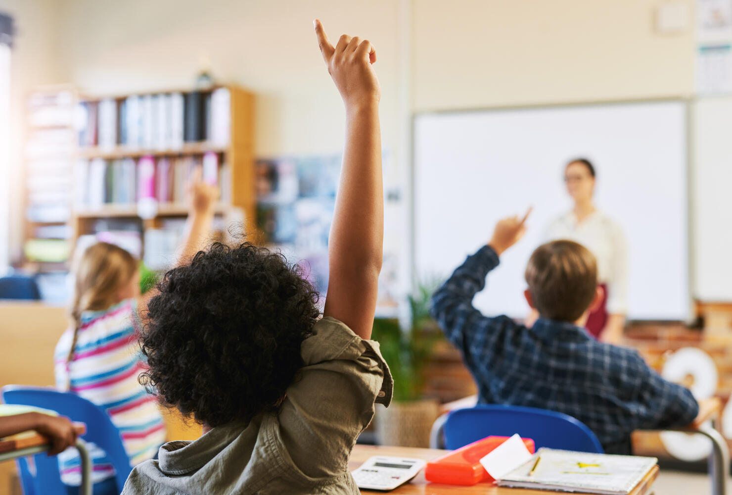 Shot of an unrecognizable group of children sitting in their school classroom and raising their hands to answer a question