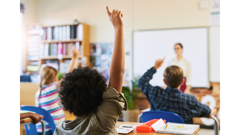 Shot of an unrecognizable group of children sitting in their school classroom and raising their hands to answer a question