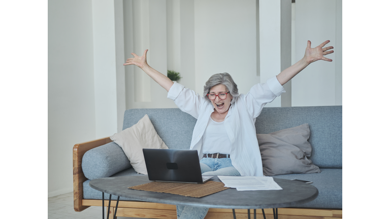 An excited senior woman is actively rejoicing and expressing her emotions about winning the online lottery