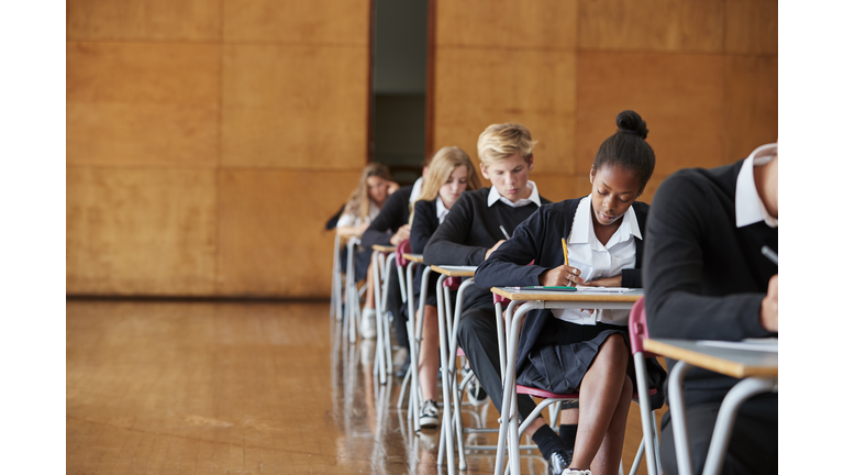 Teenage Students In Uniform Sitting Examination In School Hall