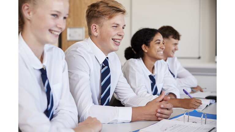 Line Of High School Students Wearing Uniform Sitting At Desk In Classroom