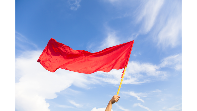 Hand waving a red flag with blue sky background