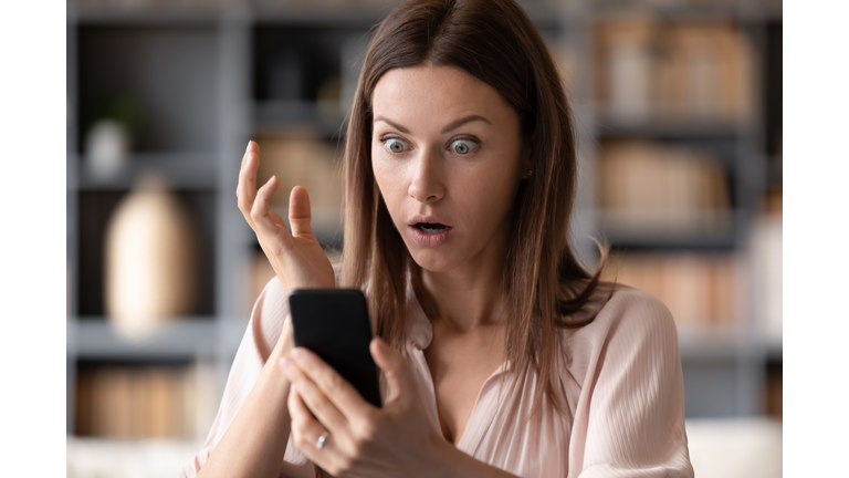 Close up young shocked woman looking at mobile phone screen.