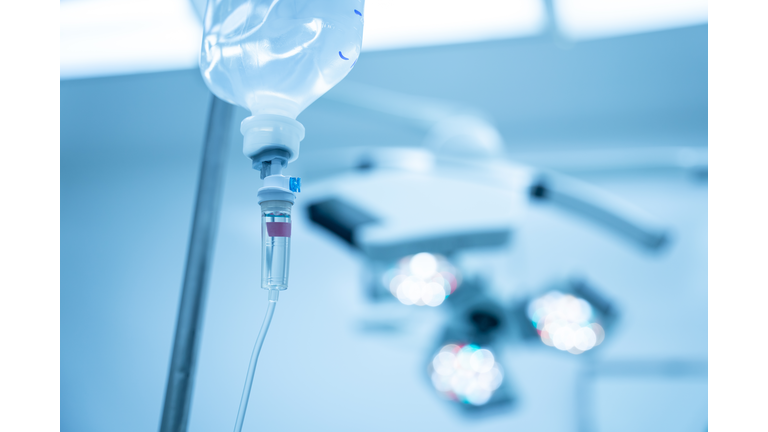 Saline syringe pump with blurred background.Intravenous fluid used in the operating room while doctor perform surgery. Surgical lamp in background with red highlight. Medical concept.