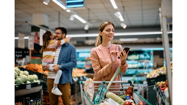 Mid adult woman using mobile app while shopping in supermarket.