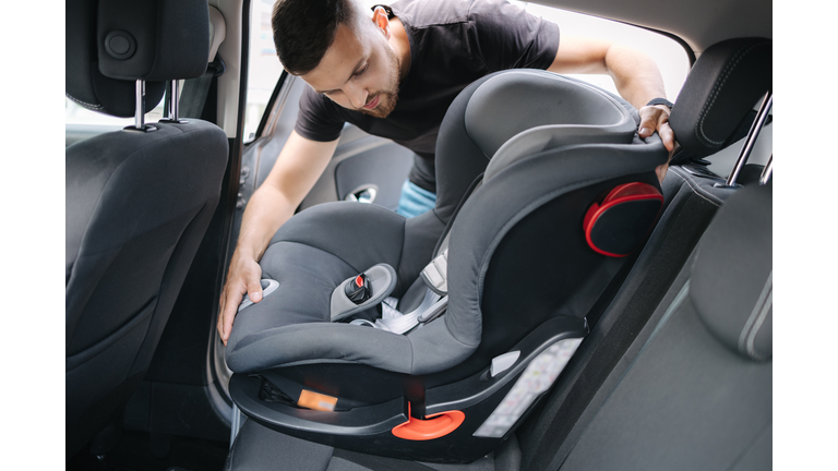 Man installs a child car seat in car at the back seat. Responsible father thought about the safety of his child