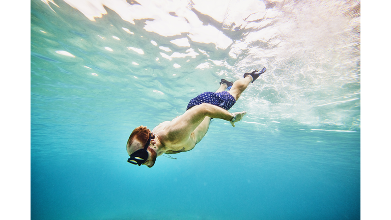 Wide shot underwater view of man snorkeling in tropical sea