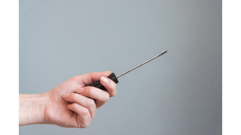woman holding a screwdriver in her hand on gray background.