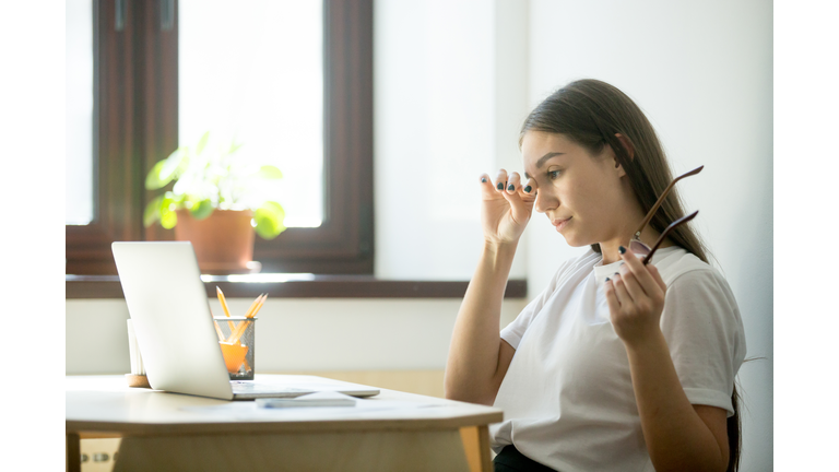 Tired businesswoman holding glasses and rubbing eyes in home office