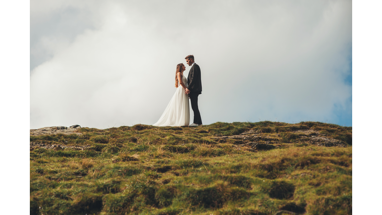 Side view of loving wedding couple standing on grassy hill and holding hands while looking at each other. Side view. Holiday wedding. Top view, lifestyle. Beautiful girl. The concept of holding a wedding in nature, love, family and relationships