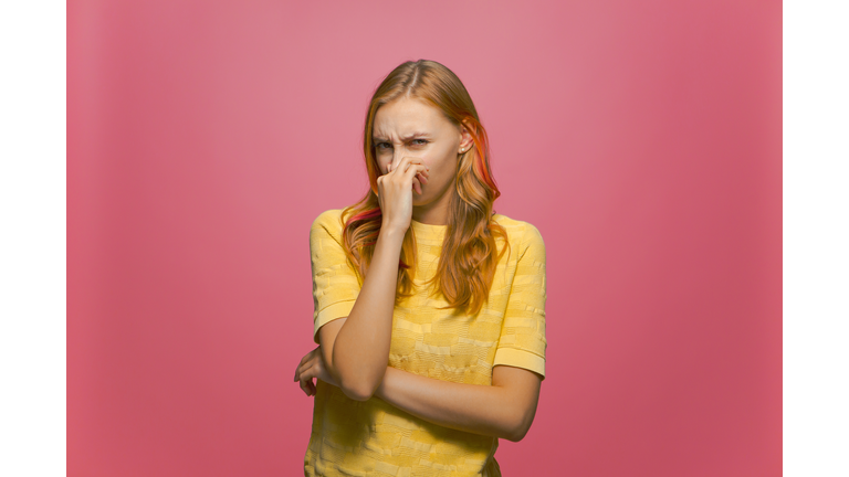 Bad smell. Young girl holding breath with fingers on nose from stinky odor on pink studio background. Parosmia problem