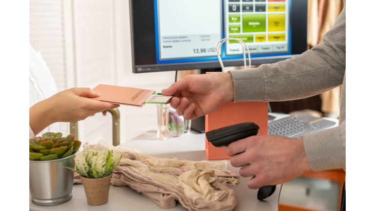 Woman holding out passport with boarding pass to cashier in female boutique store at the airport duty free.