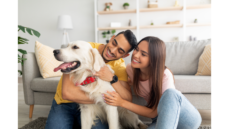 Portrait of happy multiracial couple scratching their pet dog, sitting on floor at home