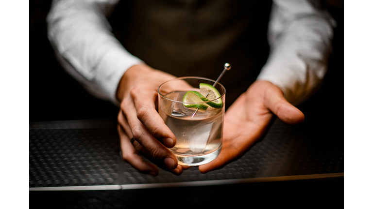 close-up on hands of man bartender holding glass with cold drink