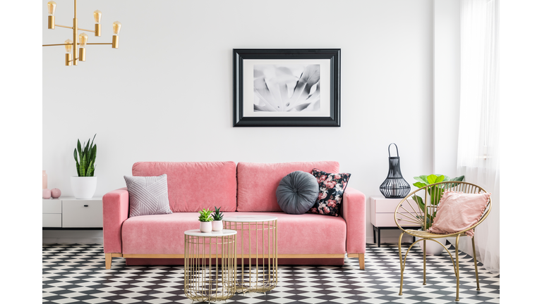 Glamour living room interior with a pink sofa, golden armchair and tables, painting and checkered tiles. Real photo