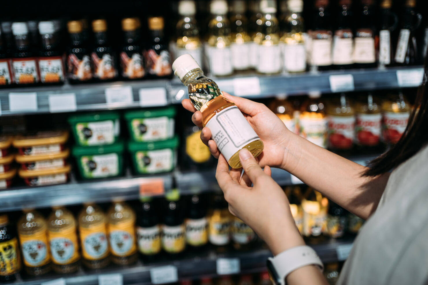 Cropped shot of young Asian woman groceries shopping in a supermarket. Standing by a produce aisle, holding a bottle of organic cooking oil and reading nutritional label