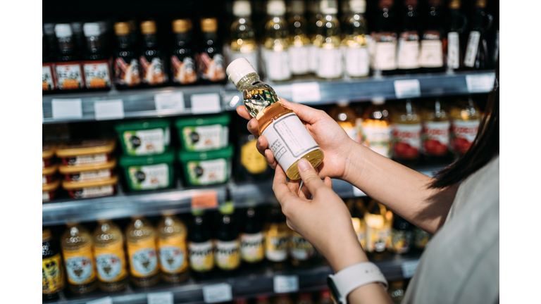Cropped shot of young Asian woman groceries shopping in a supermarket. Standing by a produce aisle, holding a bottle of organic cooking oil and reading nutritional label