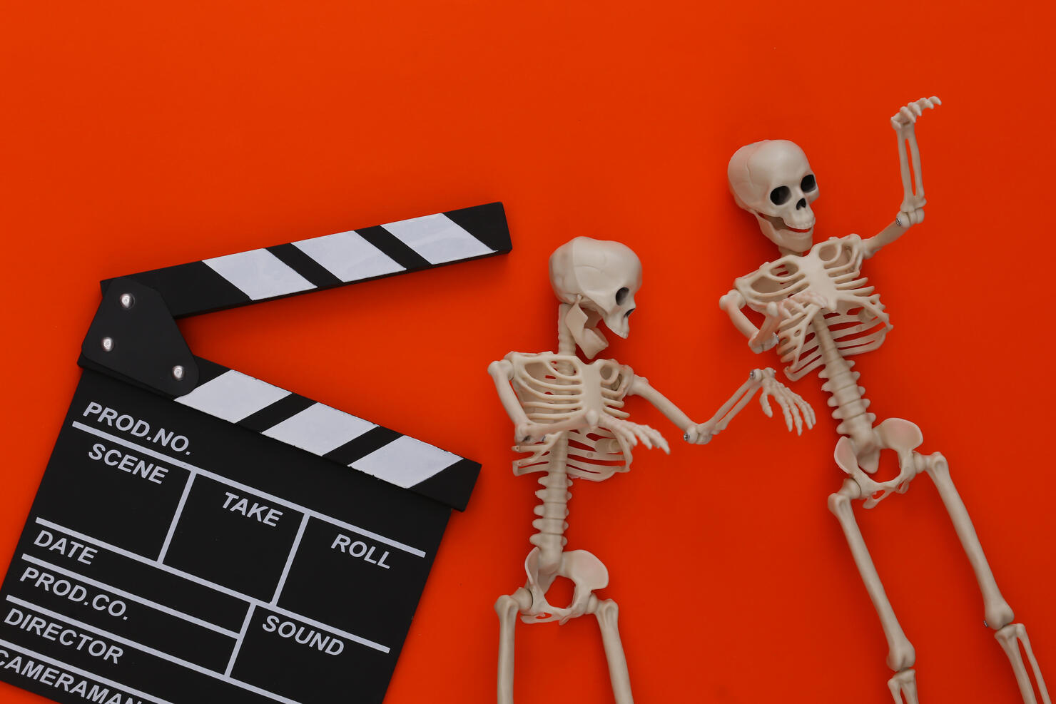 Horror movie, halloween theme. Movie clapperboard and decorative skeletons on orange background. Top view, flat lay
