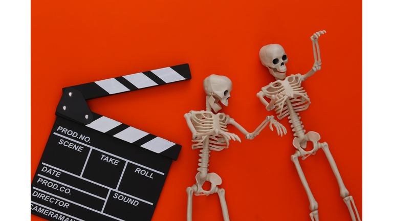 Horror movie, halloween theme. Movie clapperboard and decorative skeletons on orange background. Top view, flat lay