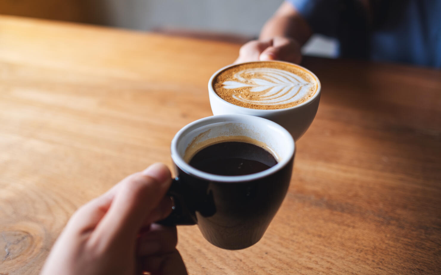 a man and a woman clinking white coffee mugs in cafe