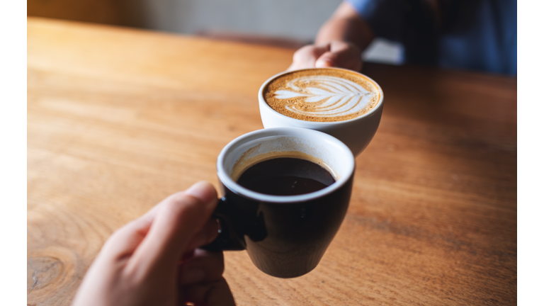 a man and a woman clinking white coffee mugs in cafe