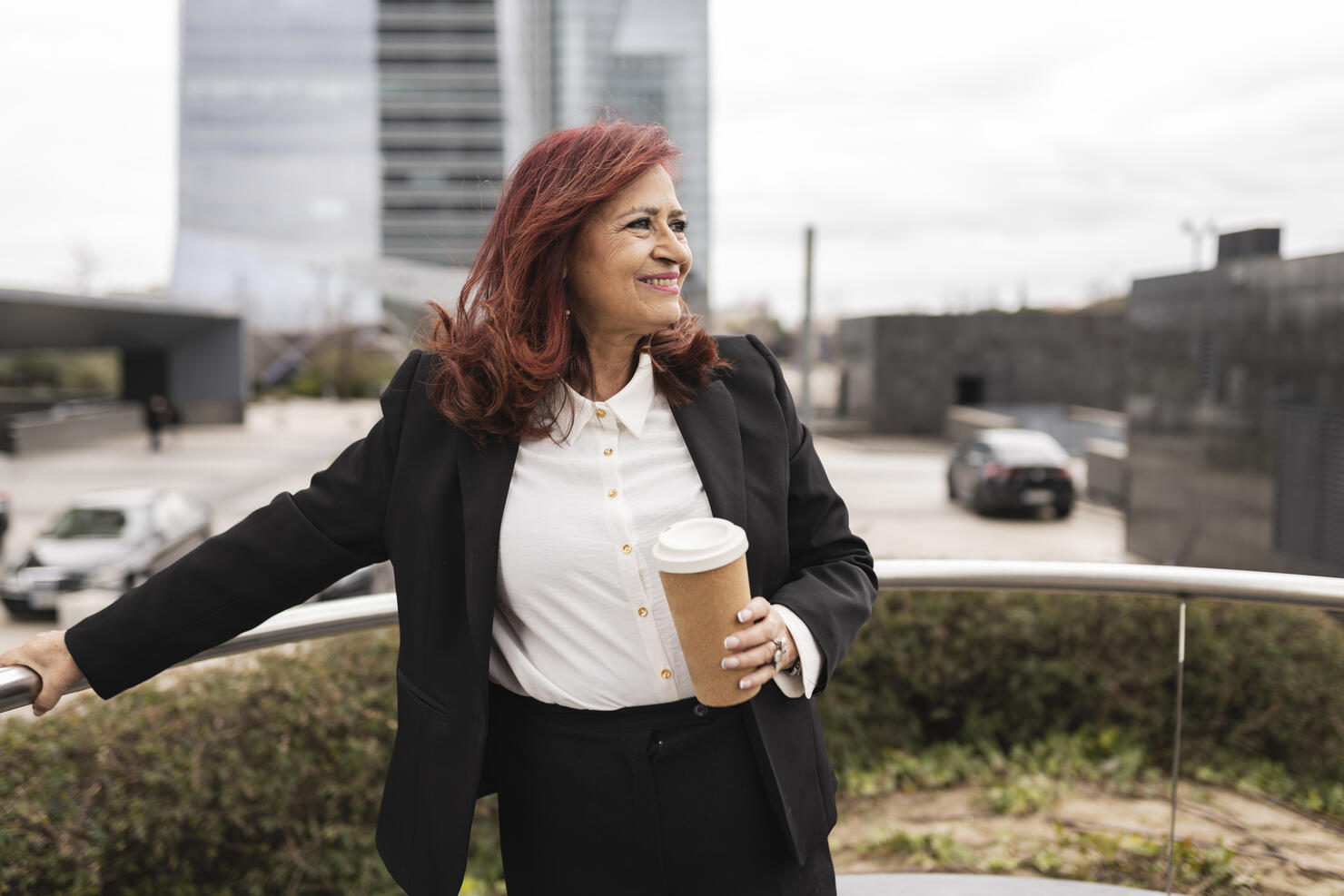 beautiful red-haired businesswoman drinking coffee from a disposable cup, in the happy city smiling and looking at the skyline
