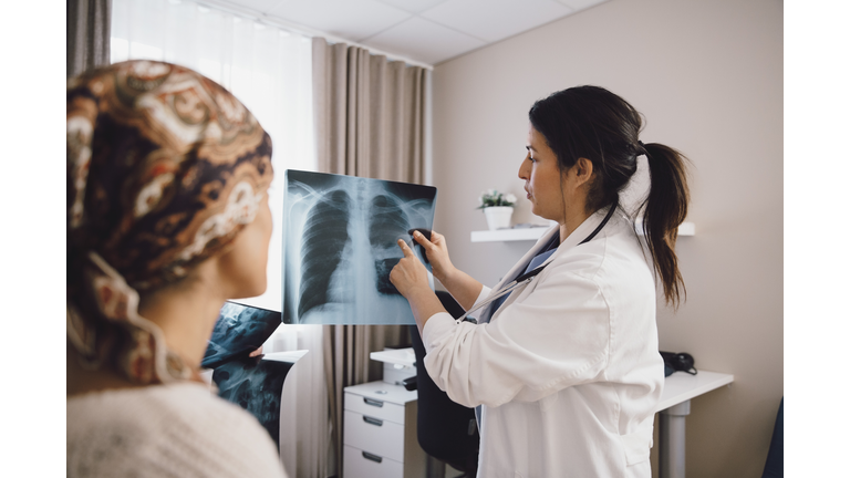 Hispanic female expertise giving advice to cancer patient while examining x-ray at doctor's office