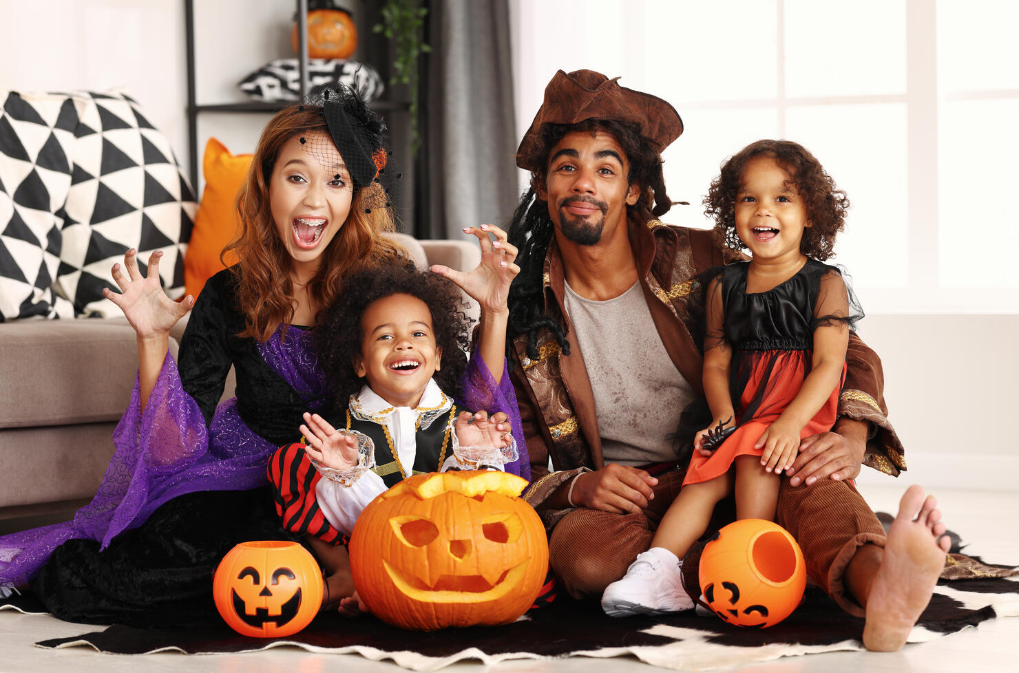 African american family in Halloween costumes making scary gesture while sitting with jack o lantern
