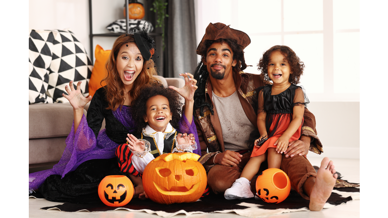 African american family in Halloween costumes making scary gesture while sitting with jack o lantern