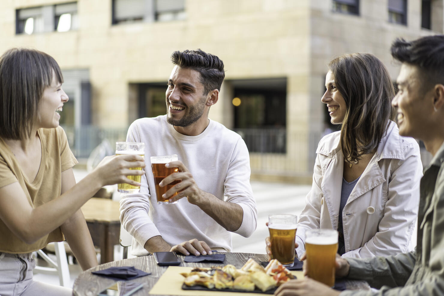 Happy friends drinking beer at the outdoor pub in the city - Friendship lifestyle concept with young millennial people enjoying time together at open air pub