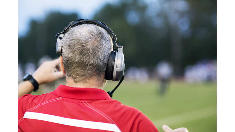 Rear view of American football coach with headphones at playing field