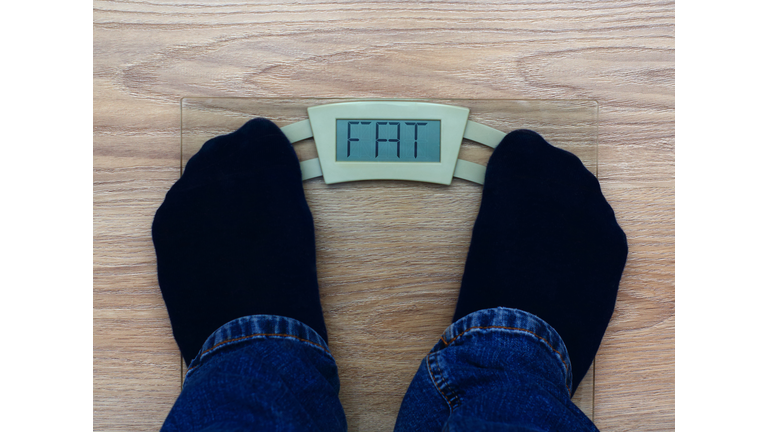 Concept of fat shaming. Man standing on weight scales with fat inscription.