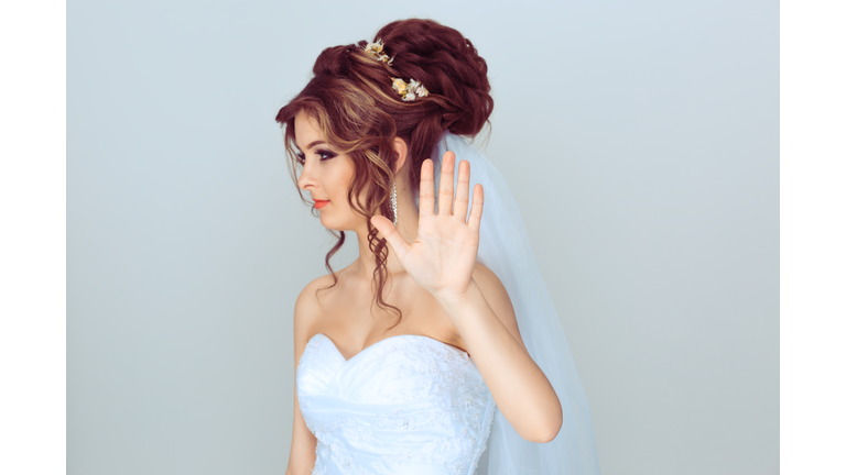 Young cool woman bride showing no stop sign with hand looking away to the side ignoring you isolated on light blue gray