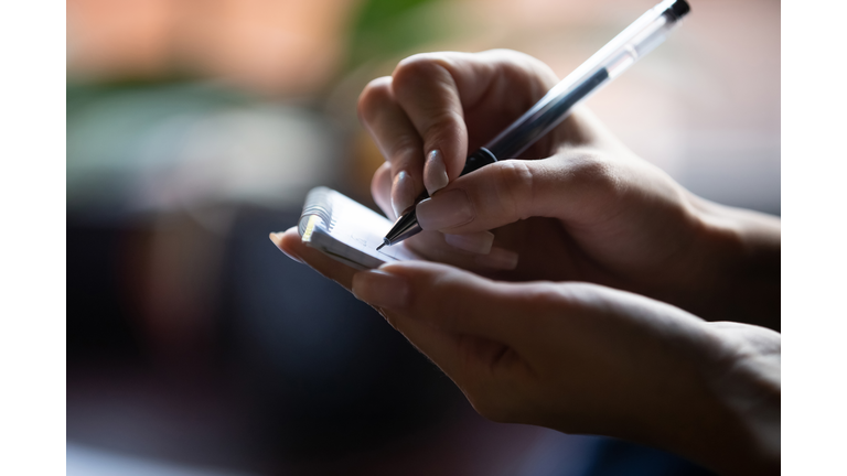 Close up hand of waitress holding pen and notepad writing visitor order