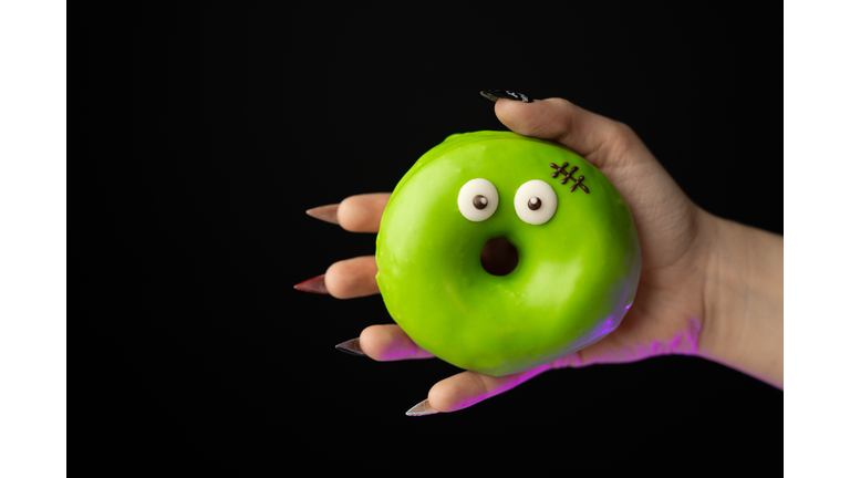 High quality hand with sharp nails holding halloween donut with surprised monster face on black background