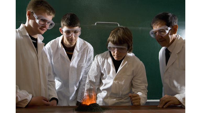 A teacher supervising students doing a chemistry experiment with lit gunpowder