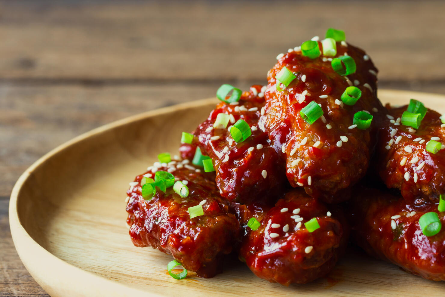 Korean fried chicken wings sprinkled with sesame and spring-onion on wood plate. Homemade Korean barbecue chicken wing delicious,moist and spicy. Fried chicken wings in Korean style on wood table.