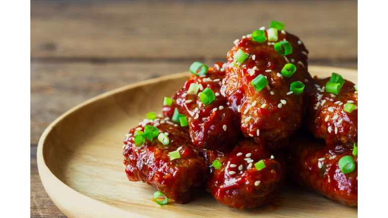 Korean fried chicken wings sprinkled with sesame and spring-onion on wood plate. Homemade Korean barbecue chicken wing delicious,moist and spicy. Fried chicken wings in Korean style on wood table.