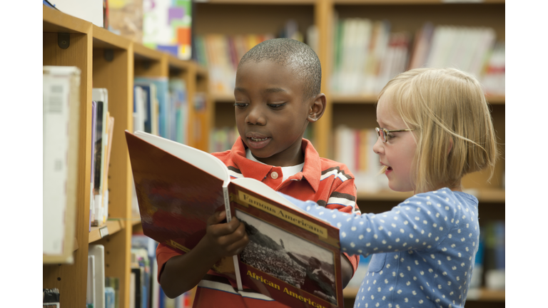 Boy and girl classmates sharing book in library