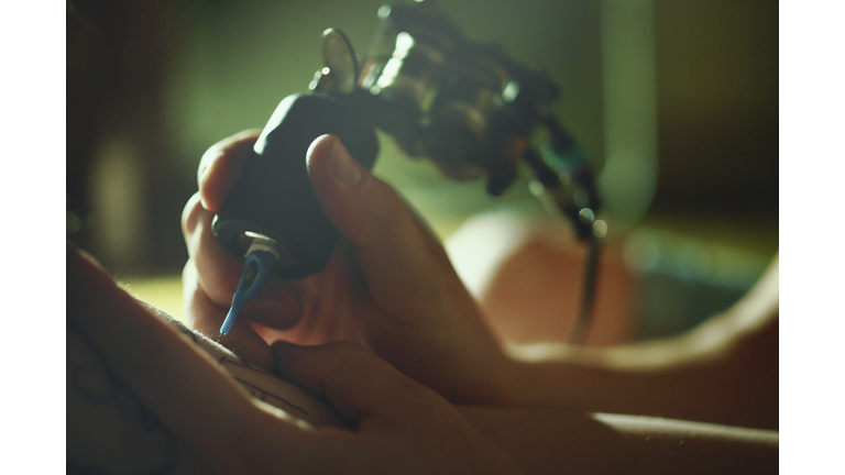 Tattoo master tattooing on the a girl arm.