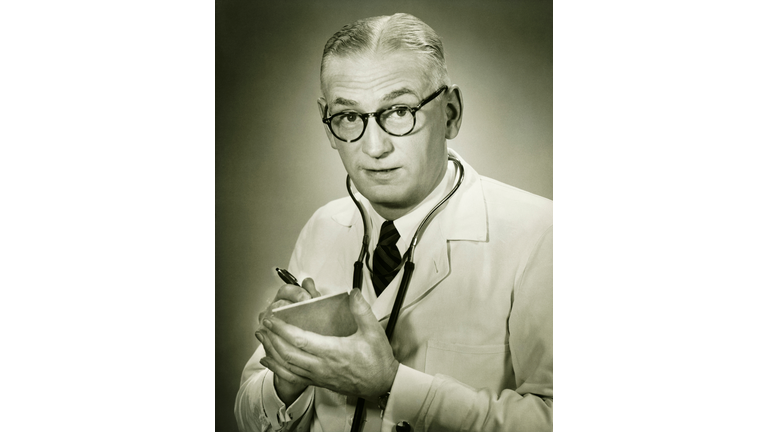 Doctor holding note pad posing in studio, (B&W), portrait