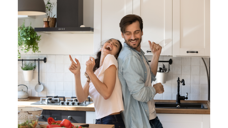 Overjoyed young family having fun in modern kitchen, dancing, laughing