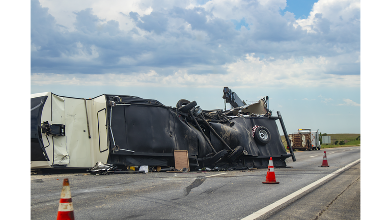 Fifth wheel Recreational Vehicle overturned on a highway with the underside torn up and things spilling out into the roadway after an accident