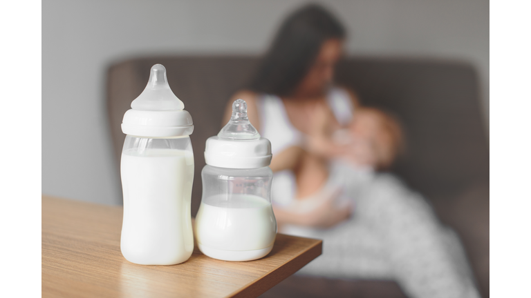 Bottles with breast milk on the background of mother holding in her hands and breastfeeding baby. Maternity and baby care.
