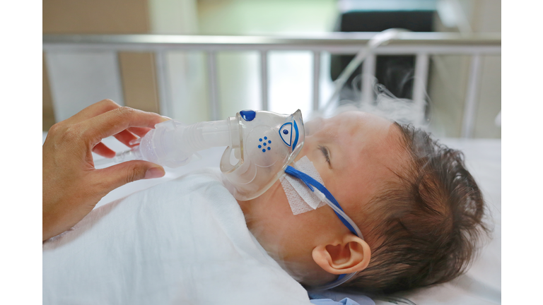 Toddler boy using nebulizer to cure asthma or pneumonia disease . Sick baby boy rest on patients bed and has inhalation therapy by the mask of inhaler. Respiratory Syncytial Virus (RSV).