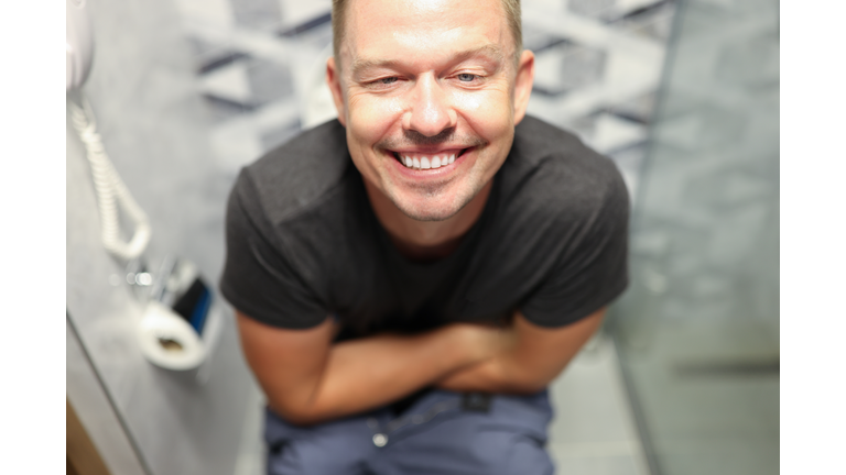 Young happy man sitting on toilet and smiling