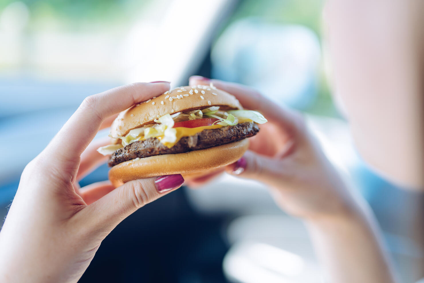 Girl holding a hamburger in  her hands sitting in a car. Unhealthy eating concept