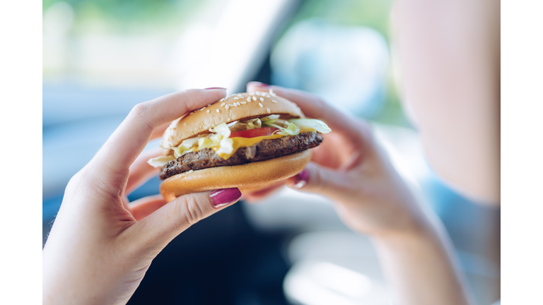 Girl holding a hamburger in  her hands sitting in a car. Unhealthy eating concept