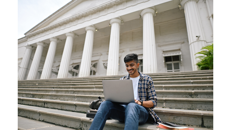 University student sitting outside on steps and using laptop